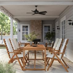 a wooden table and chairs sitting on a porch next to a house with a ceiling fan