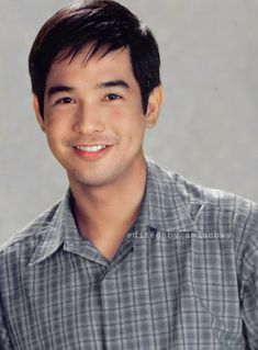 a young man smiling at the camera with his eyes wide open and wearing a plaid shirt