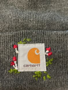 a gray beanie with red and white flowers on the side, embroidered onto it