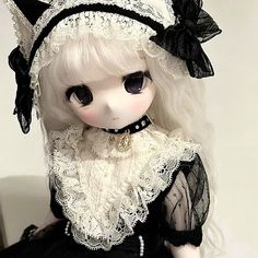 a doll with white hair wearing a black dress and lace headband, sitting on a chair