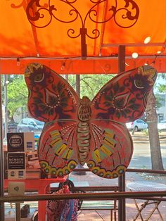 a colorful butterfly sculpture sitting on top of a red table under an orange awning