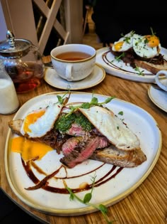 two plates with food on them sitting on a table next to cups and saucers