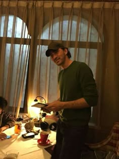 a man standing in front of a table with food and drinks on it next to a window