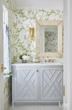 a bathroom vanity with two sinks and a large mirror above it, in front of a floral wallpaper