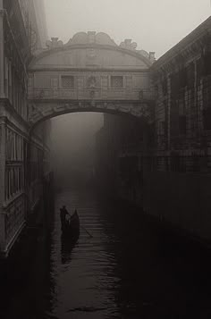 two people in a small boat on a river under an overpass with buildings and bridge