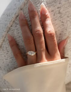 a woman's hand with a diamond ring on her finger, wearing a white coat