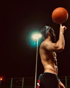 a shirtless man holding a basketball in his right hand and looking up at the sky