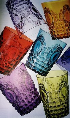 six different colored glass cups sitting next to each other on top of a white table