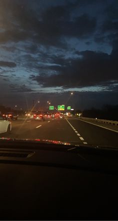 cars driving down the highway at night with dark clouds in the sky and lights on