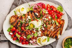 a plate with grilled meat, salad and hard boiled eggs on it next to a bowl of dressing