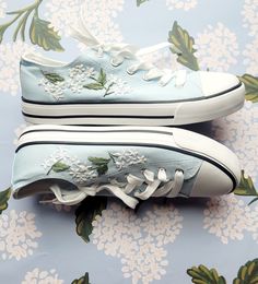 a pair of blue shoes with white flowers on them sitting on a floral wallpaper