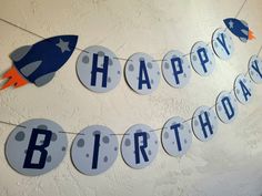 a happy birthday banner hanging from the ceiling in front of a white wall with blue and orange decorations