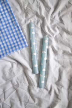 two blue candles sitting on top of a bed next to a checkered table cloth