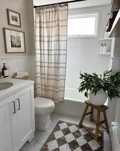 a bathroom with a checkered rug on the floor and a potted plant in the corner