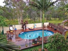 an above ground pool surrounded by palm trees and other greenery in the back yard