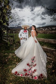 a bride and groom pose in front of a wooden fence with flowers on the grass