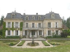 a large house with many windows and lots of plants on the front lawn, surrounded by hedges