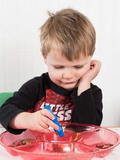 a young boy sitting at a table with a red bowl and blue spoon in front of him