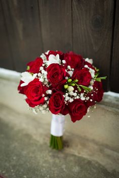 a bouquet of red roses and baby's breath is sitting on the ground in front of a wooden door