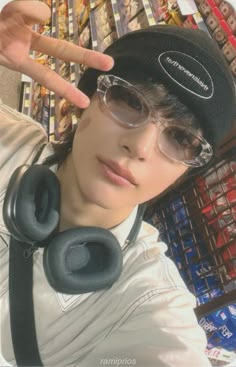 a person wearing glasses and a hat with headphones around his neck, making the peace sign