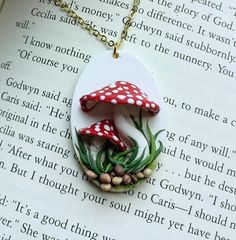 a necklace with two mushrooms on it sitting on top of a page of a book