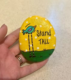 a hand holding a painted rock that says stand tall