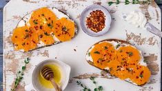 two pieces of bread with oranges and cream on them next to a bowl of honey