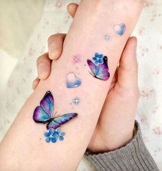 two hands with tattoos that have butterflies and hearts painted on them, one is holding the other's hand