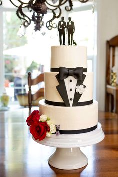 a three tiered wedding cake decorated with black and white tuxedo, bow tie, and roses