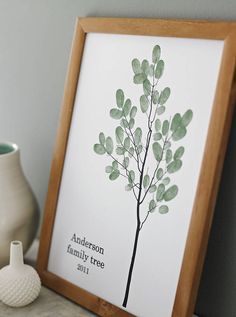 a framed print with a tree on it next to a white vase and a wooden frame