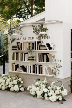 there is a book shelf with books on it and flowers in front of the shelves