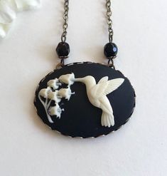 "Here is a super sweet hummingbird necklace featuring a nicely detailed cameo depicting a hummingbird with lily of the valley flowers. This cameo is black and white, it is horizontal style and set in an oxidized brass setting that is suspended from a nice quality non tarnish brass chain. You may select your desired chain length from the drop down menu. Handcrafted in the USA by Botanical Bird jewelry. Shipped in a lovely gift box and perfect for gift giving! Large Cameo Pendant measures: 1 1/4\" Black Rope Necklace, Black Cameo, Hummingbird Jewelry, Victorian Cameo, Egyptian Necklace, Hummingbird Necklace, Lily Of The Valley Flowers, Hummingbird Pendant, Valley Flowers