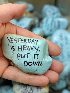 a hand holding a rock with writing on it that says, yesterday is heavy put it down