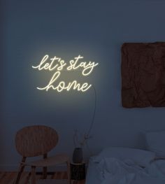 a neon sign that says let's stay home on the wall above a bed