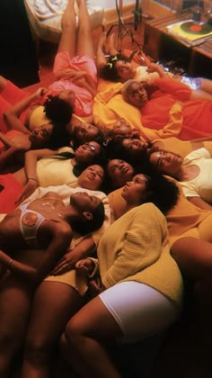 several women laying on top of each other in the middle of a bed with orange sheets