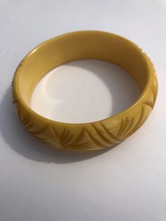 Stunning, fresh from estate piece! This gorgeous Bakelite bangle has all the right details. This piece is a warm buttery yellow. It has a carved design all the way around of alternating diagonal lines and trips of organic gently curving and bending lines reminiscent of grasses or palm fronds. In very good condition with just the right amount of minimal wear. This feels like the original owners favorite piece as it shows a slight bit more evidence of wear in the form of a few dark scuffs and mino Vintage Yellow Gold Bangle, Vintage Yellow Round Bracelets, Vintage Yellow Gold Bangle Cuff Bracelet, Yellow Bangle Bracelets For Formal Occasion, Vintage Handmade Yellow Gold Bracelet, Handmade Vintage Yellow Gold Bracelet, Classic Yellow Bracelet, Vintage Bakelite Bangle Jewelry, Vintage Bakelite Bangle