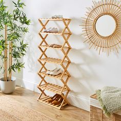 a bamboo shoe rack next to a potted plant in a room with a round mirror on the wall