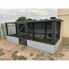 a large chicken coop in the middle of a dirt field with a fence around it