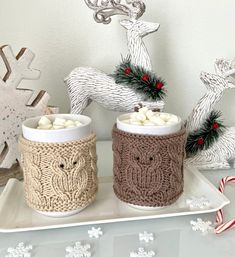 two mugs with marshmallows in them on a tray next to christmas decorations