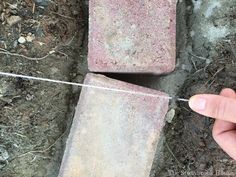 a hand is holding a string attached to two brick blocks on the ground with dirt around them