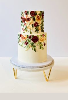 a white cake with red and yellow flowers on it sitting on a stand in front of a wall