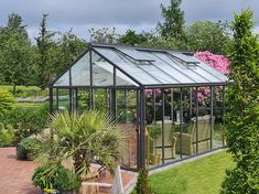 a glass house in the middle of a garden with potted plants and flowers around it