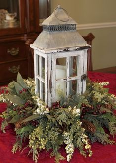 a white lantern on top of a table with greenery and pine cones around it