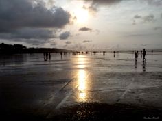 people walking on the beach at sunset with clouds in the sky and sun reflecting off the wet sand