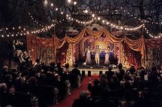 people are standing in front of a stage with lights strung from the ceiling and drapes