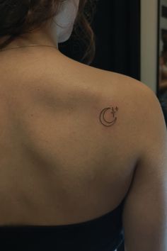 the back of a woman's shoulder with a small crescent tattoo on her left shoulder