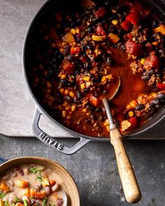 a pot filled with chili and corn next to a wooden spoon