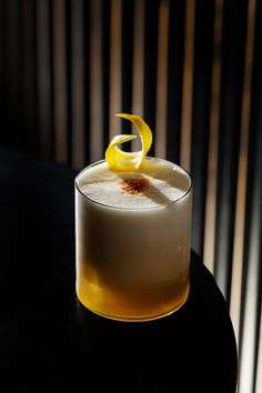 a small glass filled with liquid sitting on top of a black table next to a wooden wall