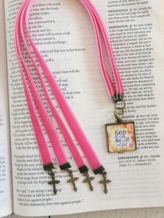 three pink necklaces with cross charms on top of an open bible, next to it is a book