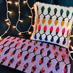 a crocheted blanket and pillow on a couch with christmas lights strung around it